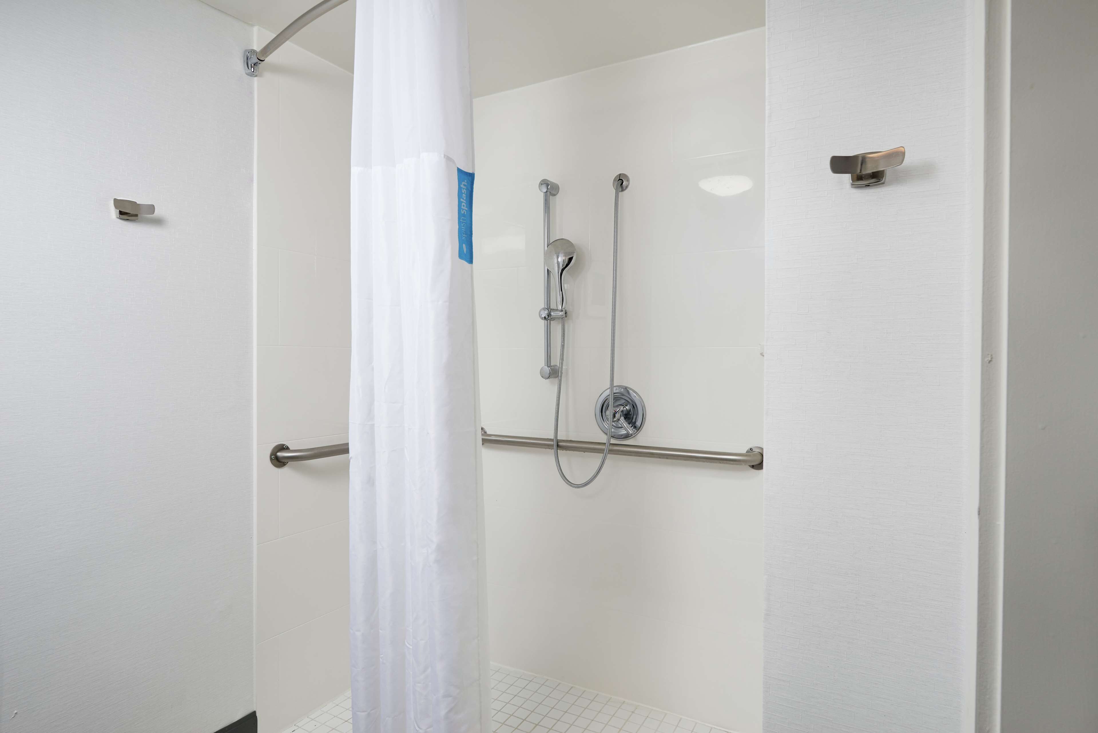 A shower area with a glass door, a showerhead, and a handrail.