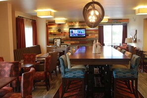 Un comedor con una mesa de madera larga, sillas estampadas y un televisor montado en la pared.