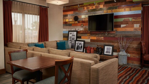 Ein Wohnzimmer mit einer Eckcouch, einem Holzesstisch und Stühlen. An einer Holzwand ist ein Flachbildfernseher angebracht.
