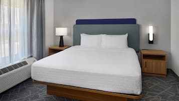 A hotel room with a bed, bedside tables, a lamp, a wall-mounted light, and a window with curtains.