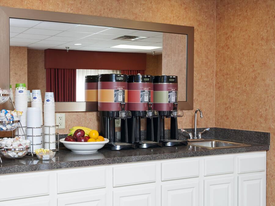 Un coin cuisine avec un espace dédié au café, un saladier rempli de fruits et une pile d’assiettes.
