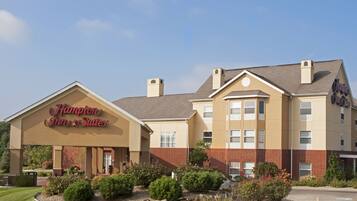Ein Hampton Inn & Suites Hotel mit Backsteinfassade, zahlreichen Fenstern und einem gepflegten Vorgarten.