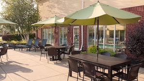 An outdoor patio with tables and chairs, green umbrellas, and a brick building in the background.