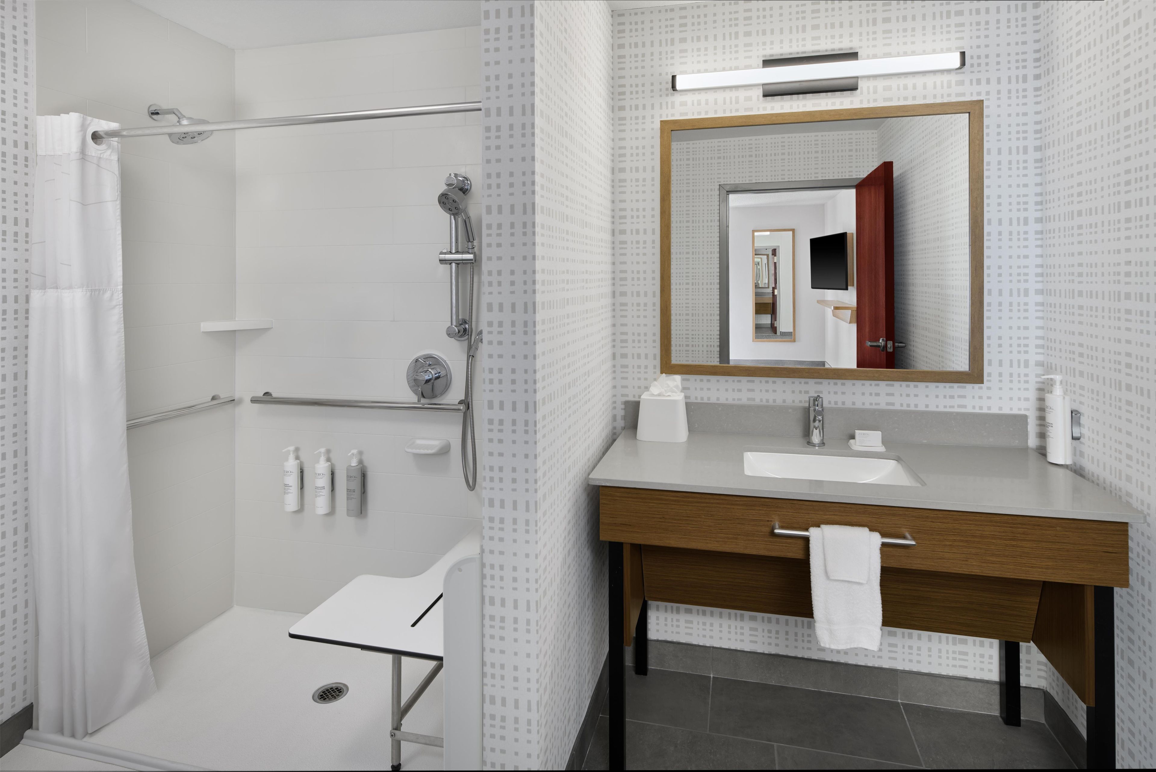 Ein modernes Badezimmer mit Dusche, Toilette und Waschbecken, ausgestattet mit einem Spiegel, einem Handtuchhalter und Toilettenartikeln.