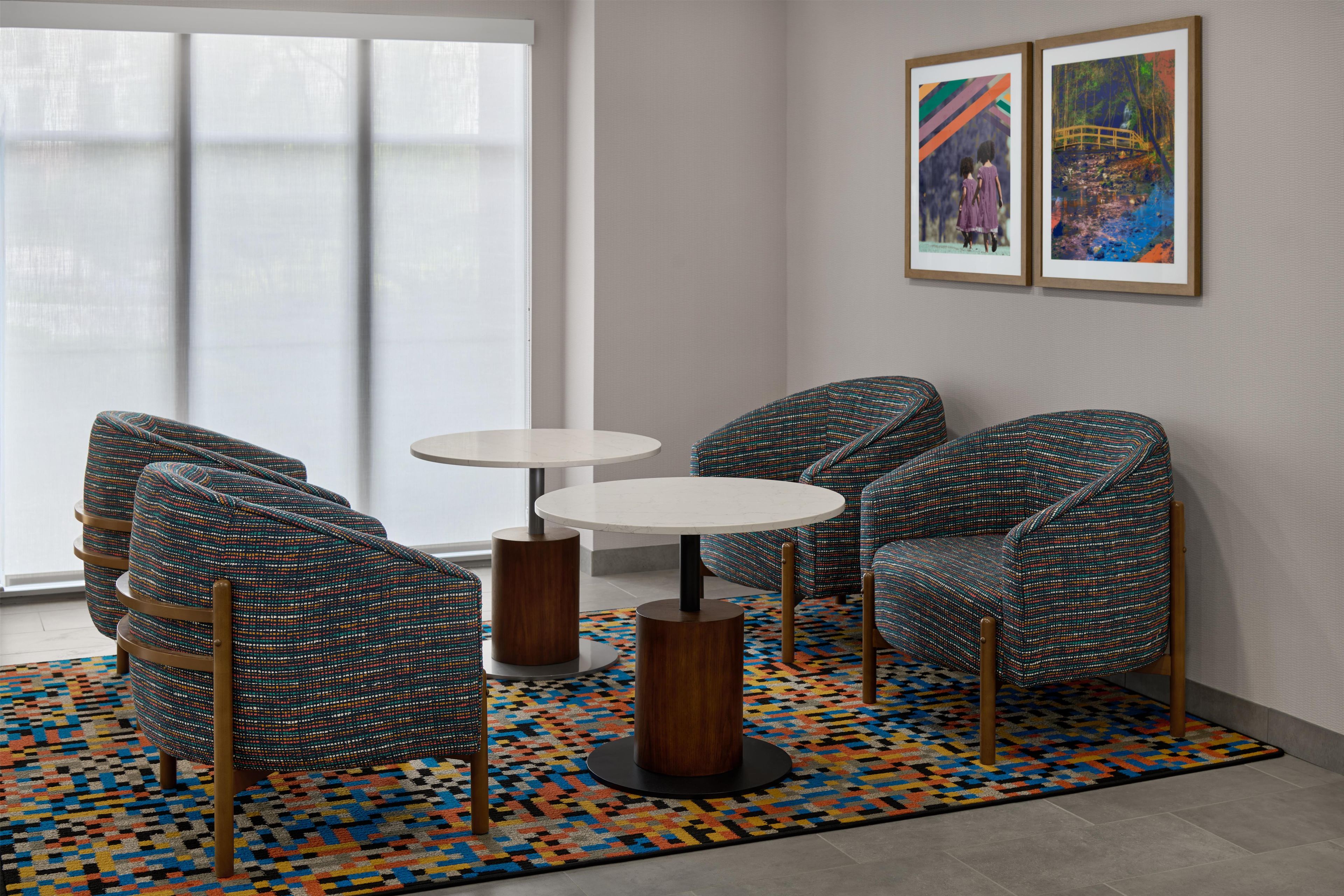A room with a patterned rug, two round tables, and four upholstered chairs with wooden legs.