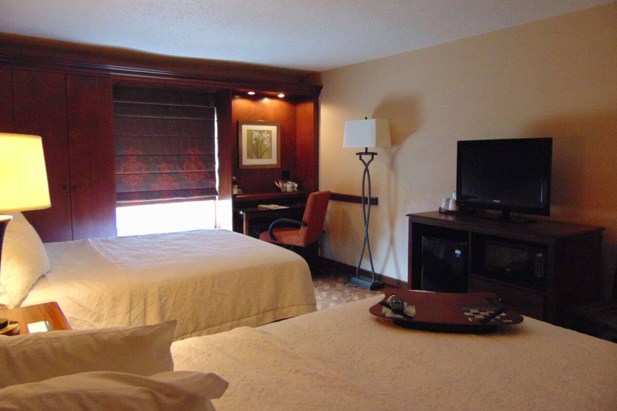 Une chambre d’hôtel avec deux lits, un bureau, une chaise, une télévision et une lampe sur pied.