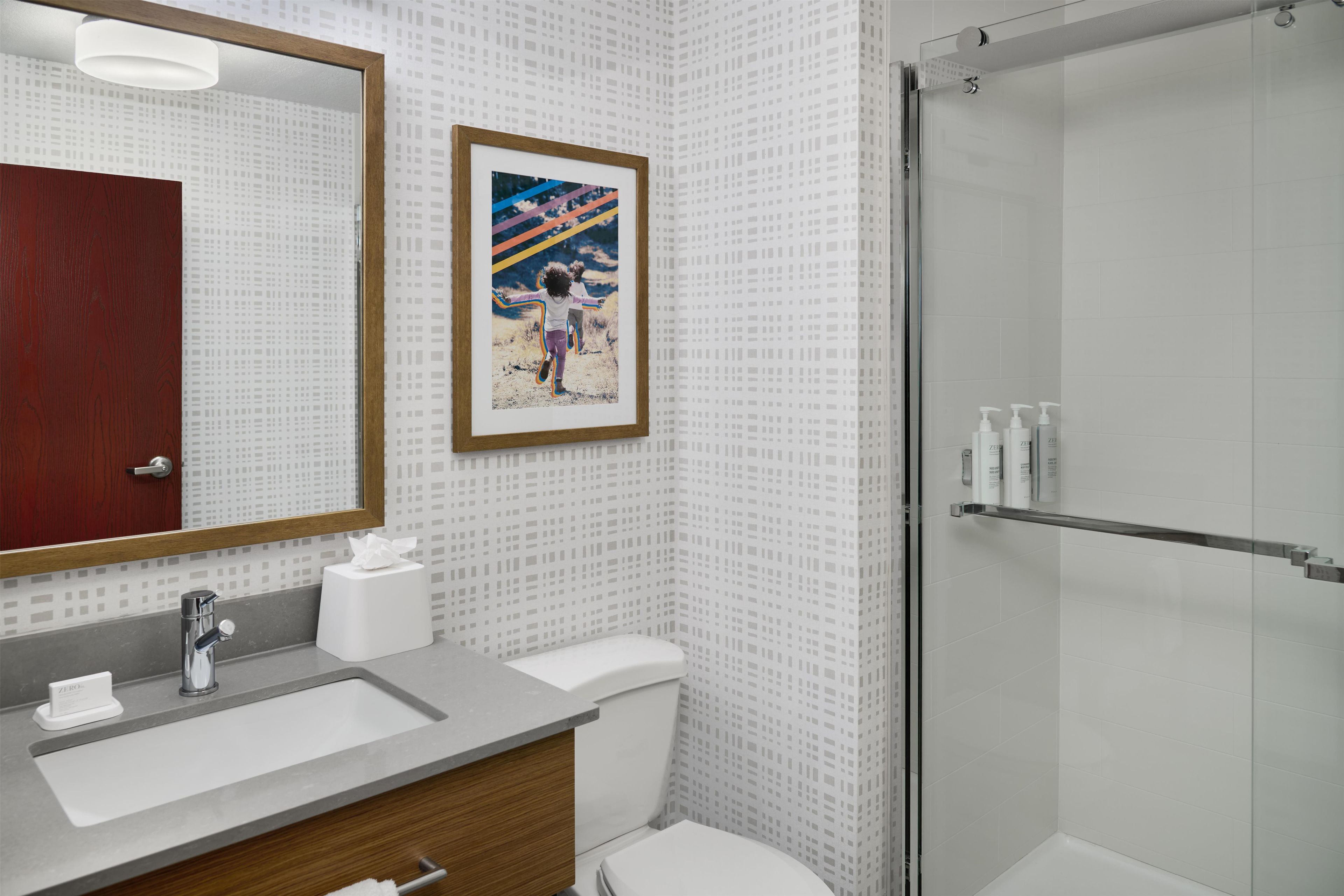 A bathroom with a sink, mirror, toilet, and shower.