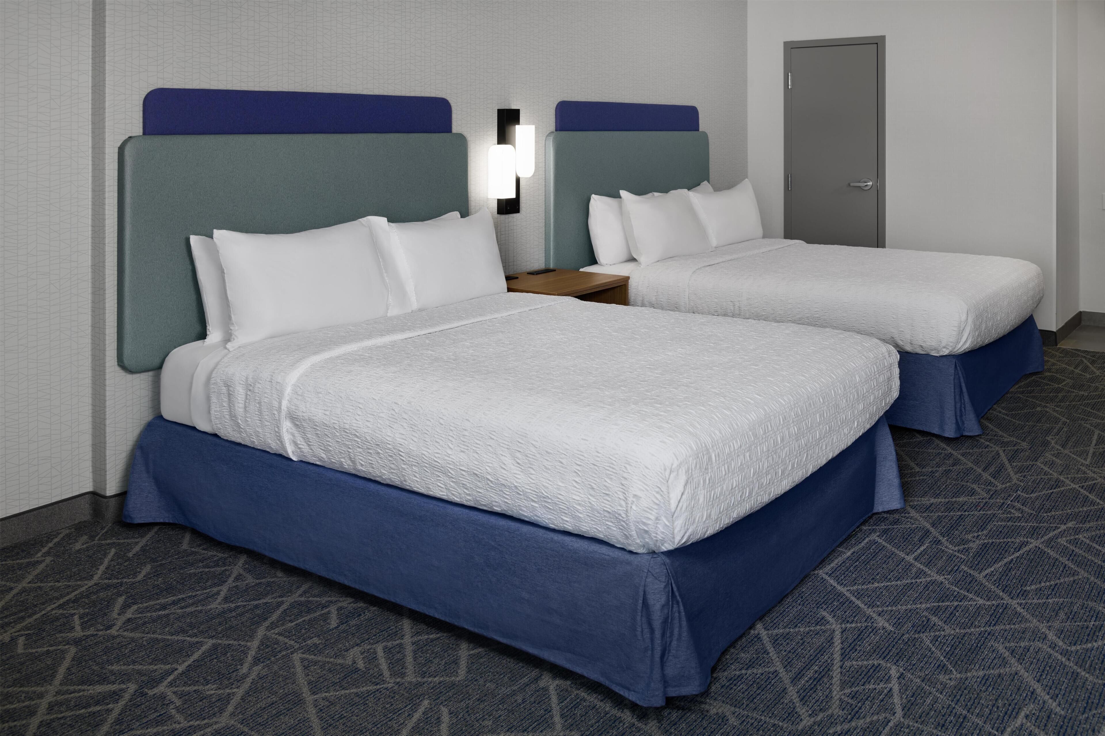 A hotel room with two beds, a nightstand, and a door.
