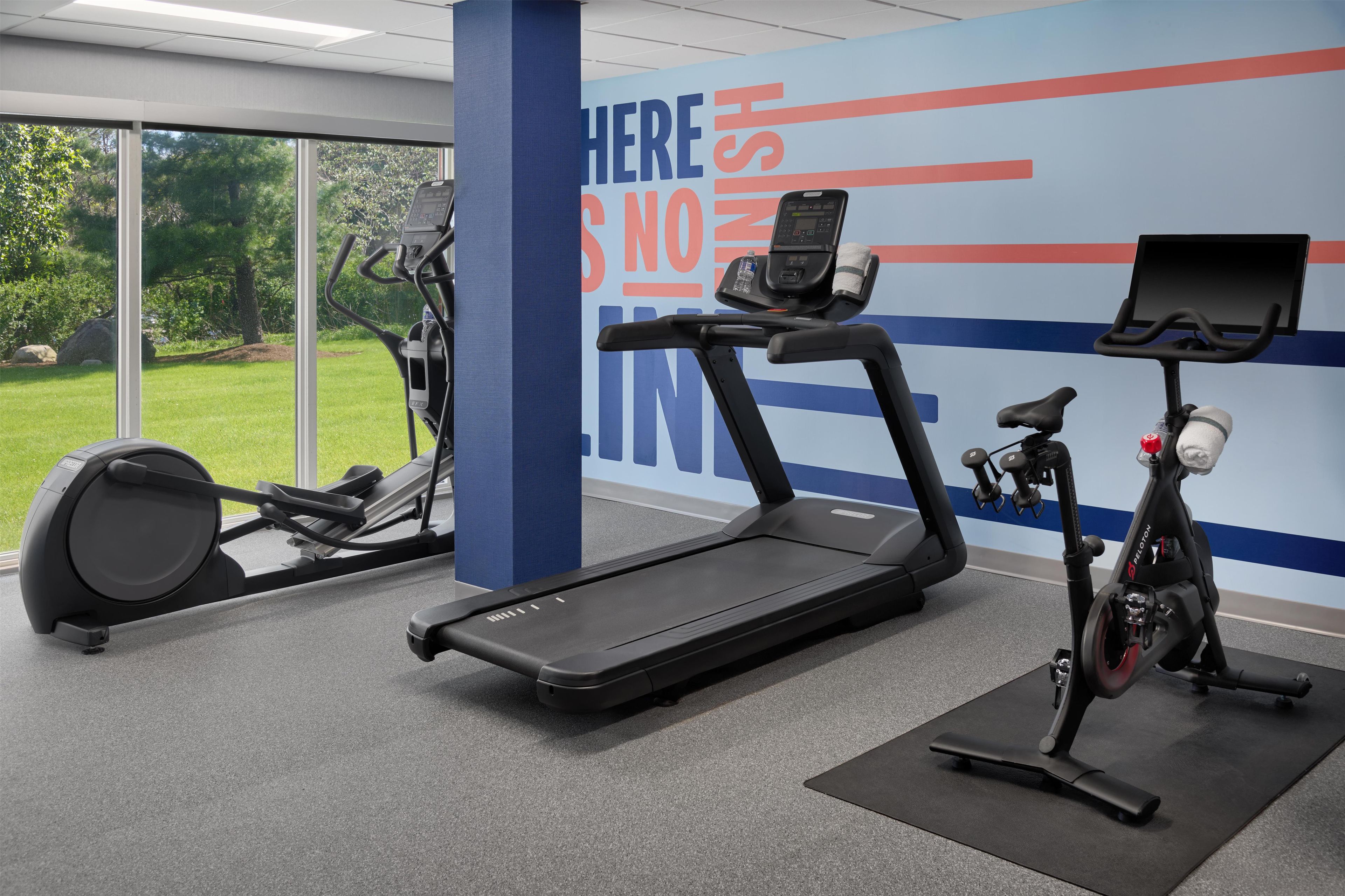 A gym with a treadmill, elliptical, and stationary bike, large windows, and a motivational wall.