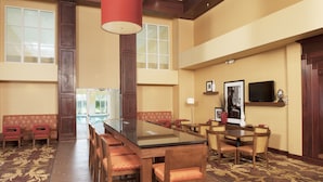 A spacious conference room with a long table, multiple chairs, a large window, and a television on the wall.