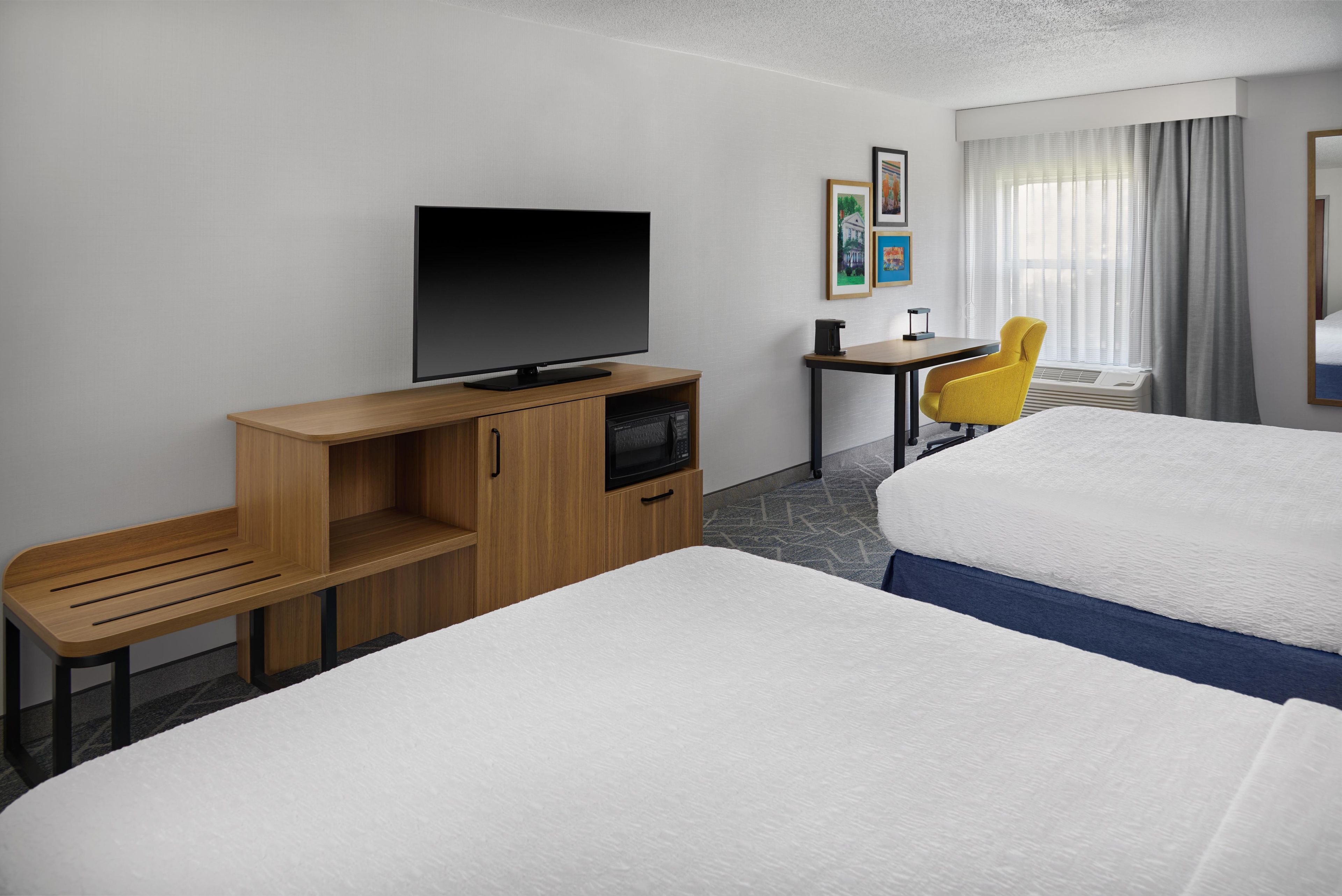 A hotel room with two beds, a TV, a desk, a chair, and a window with curtains.