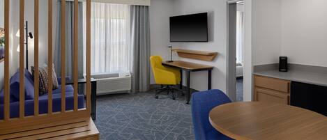 A hotel room with a wooden partition, a sofa, a desk with a chair, a TV mounted on the wall, and a dining table.
