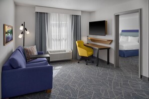 A hotel room with a sofa, a desk, a chair, a bed, a flat-screen TV, and a window with curtains. - Hampton Inn & Suites Cleveland Southeast/Streetsboro (Streetsboro)