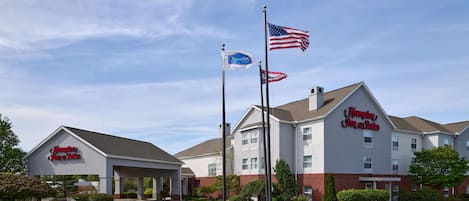 A Hampton Inn & Suites hotel with a parking lot, flagpoles, and a clear sky.