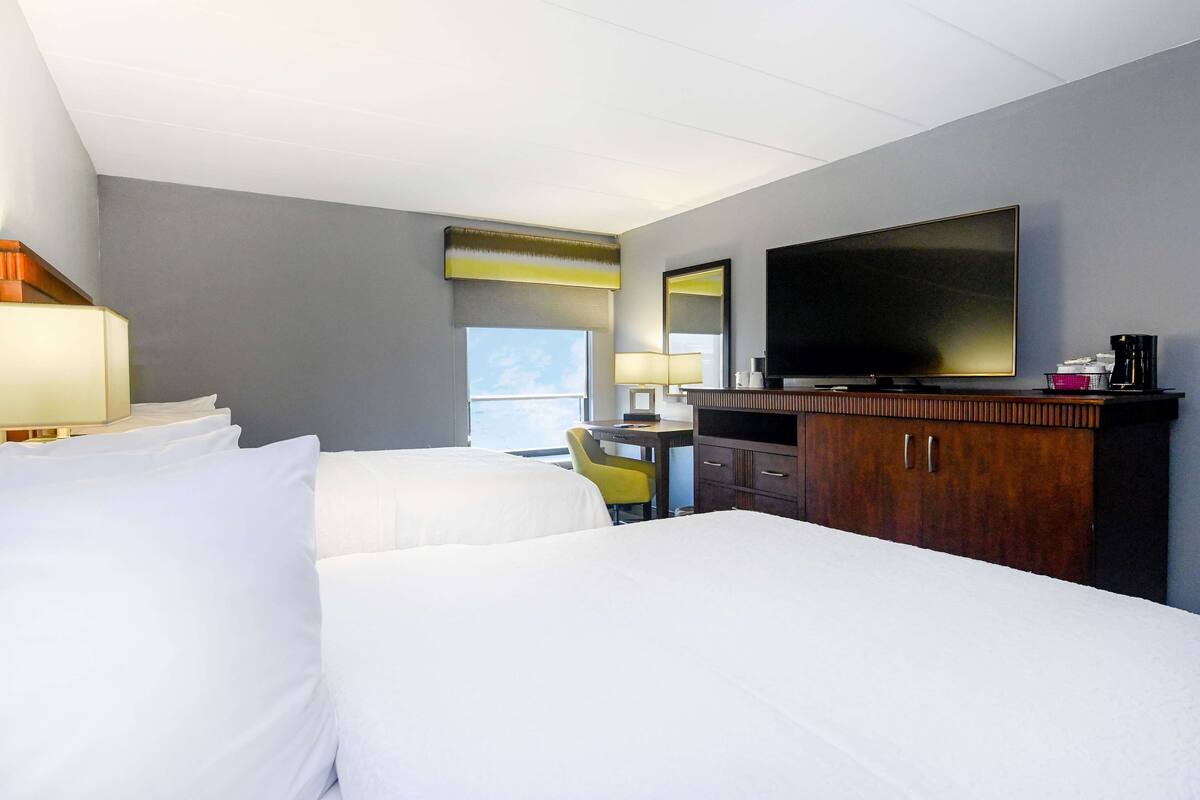 A hotel room with two beds, a desk with a chair, a television, and a minibar.