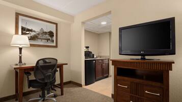 A hotel room with a desk, chair, TV, and a kitchen area with a microwave and refrigerator.