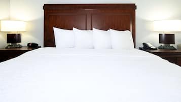 Habitación de hotel con una cama grande, cabecera de madera, ropa de cama blanca, dos mesitas de noche con lámparas y teléfonos.