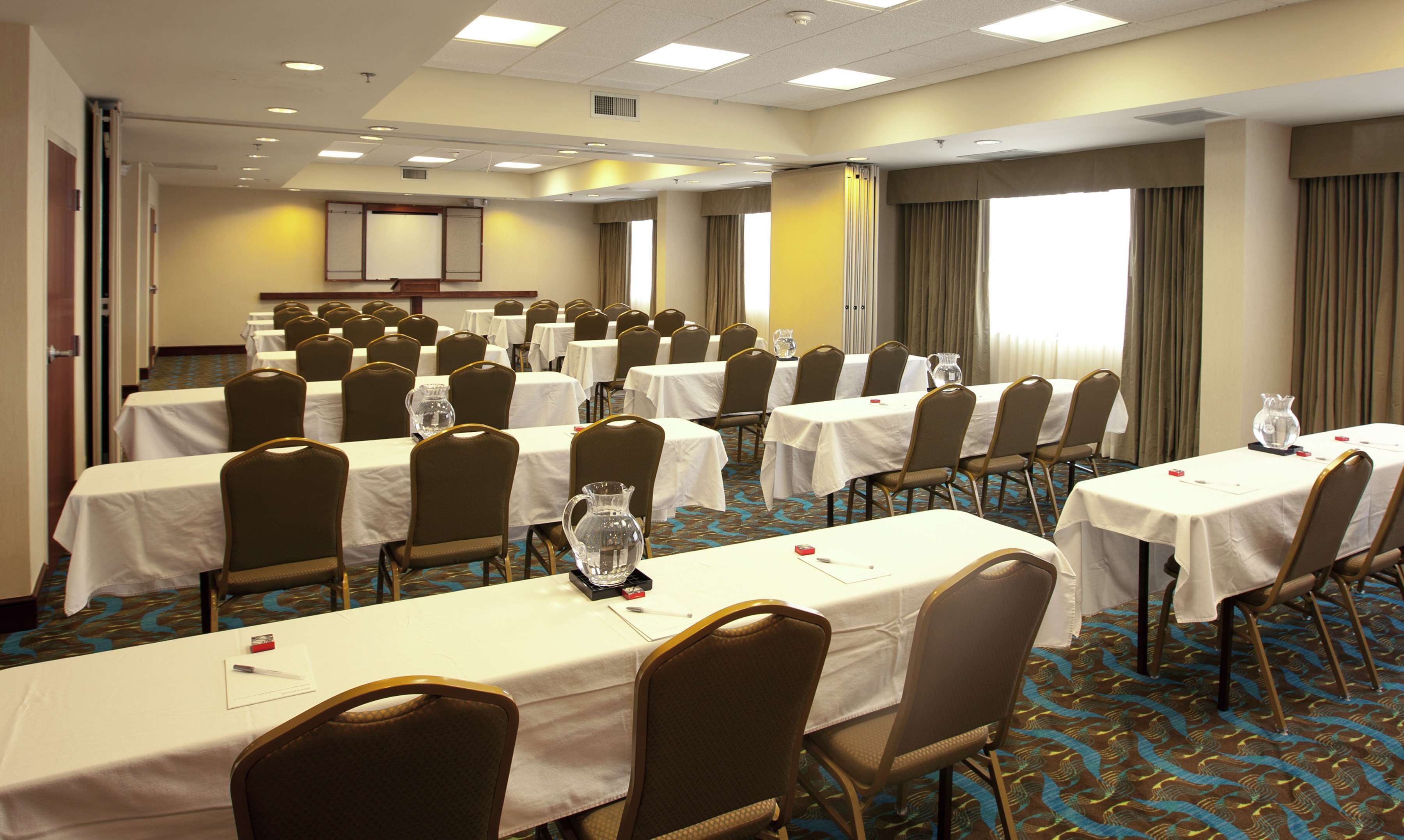 Un salón de conferencias con varias mesas y sillas, dispuestas en filas.