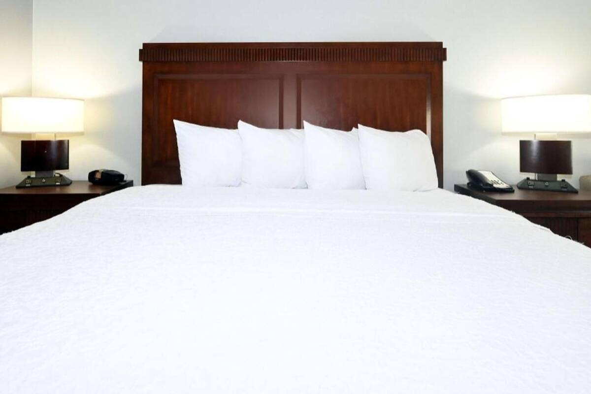 A hotel room with a large bed, wooden headboard, white bedding, two bedside tables with lamps, and a telephone on each table.