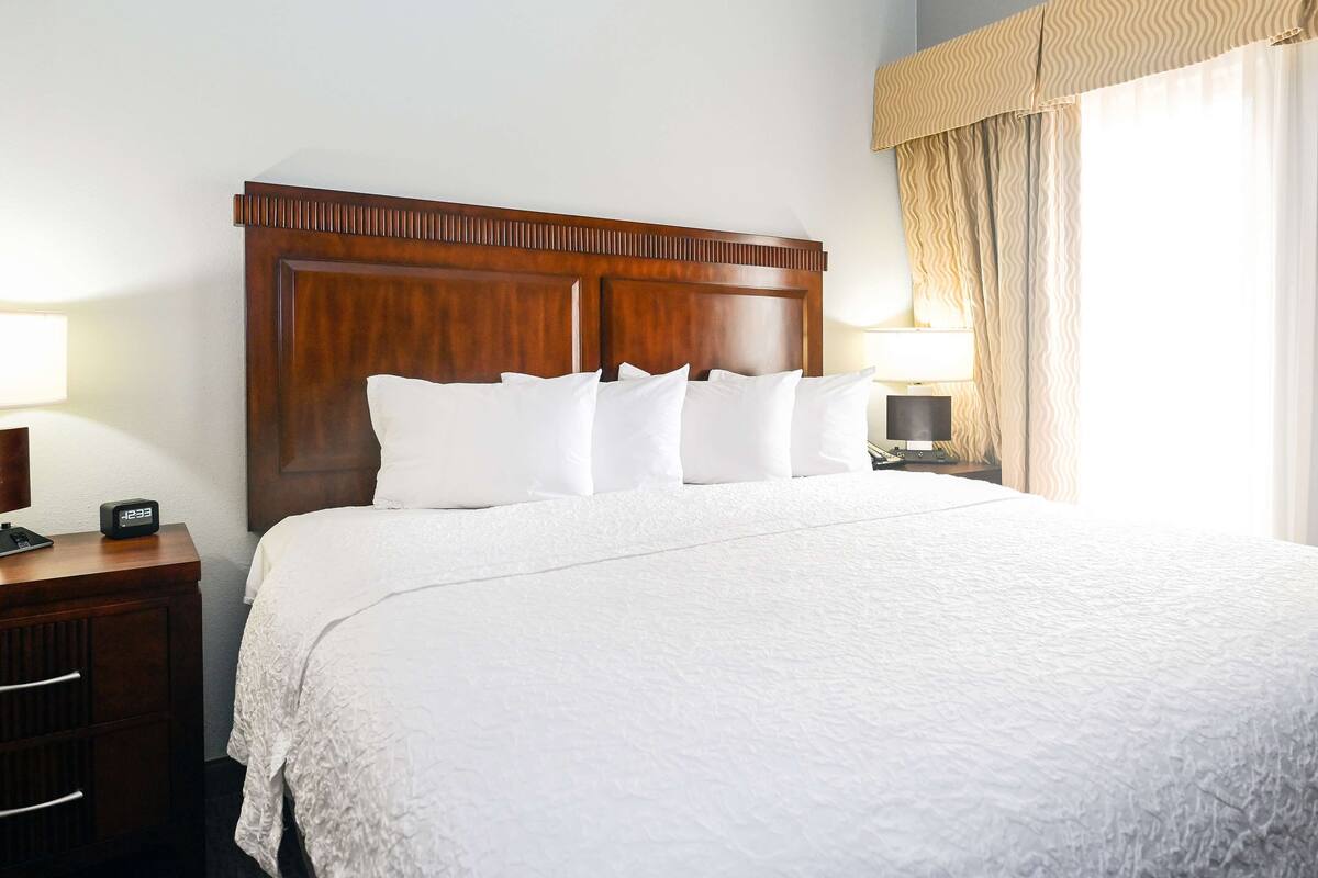 A neatly made bed with a wooden headboard, white bedding, and a bedside table with a lamp.