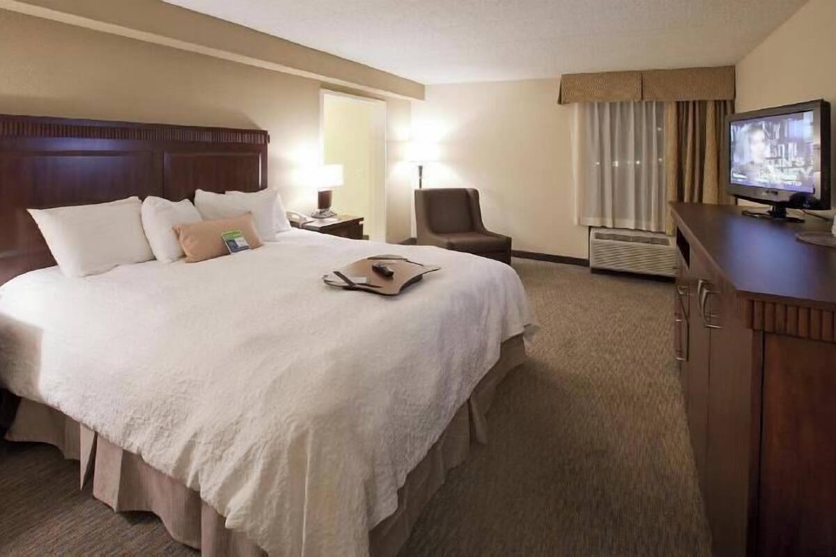 A hotel room with a large bed, a TV, a chair, and a desk.