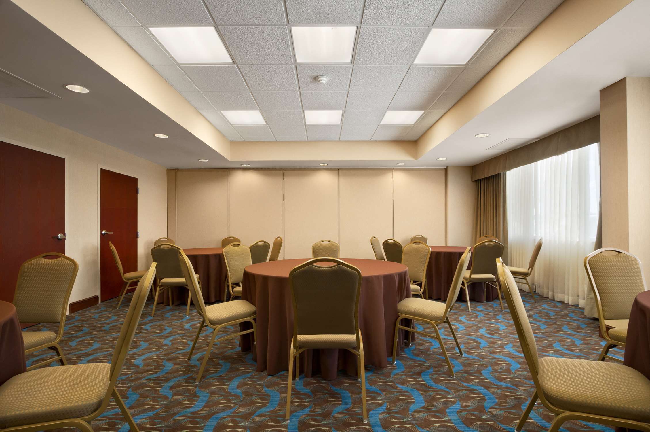 Un salón de conferencias con mesas y sillas redondas, alfombra estampada e iluminación empotrada en el techo.