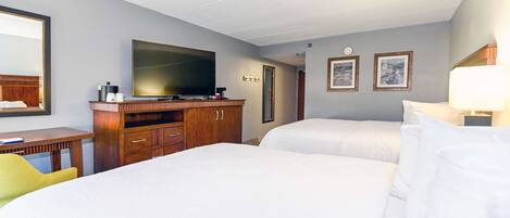 A hotel room with two beds, a TV, a desk with a chair, and a wooden dresser.