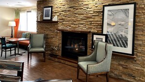 A living room with a stone wall, a fireplace, and framed pictures. - Hampton Inn by Hilton Lexington Park (Lexington Park)