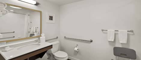 Een moderne badkamer met een wit wastafel, toilet en douche. Er is een spiegel, handdoekhouder en een rolstoel toegankelijke stoel.