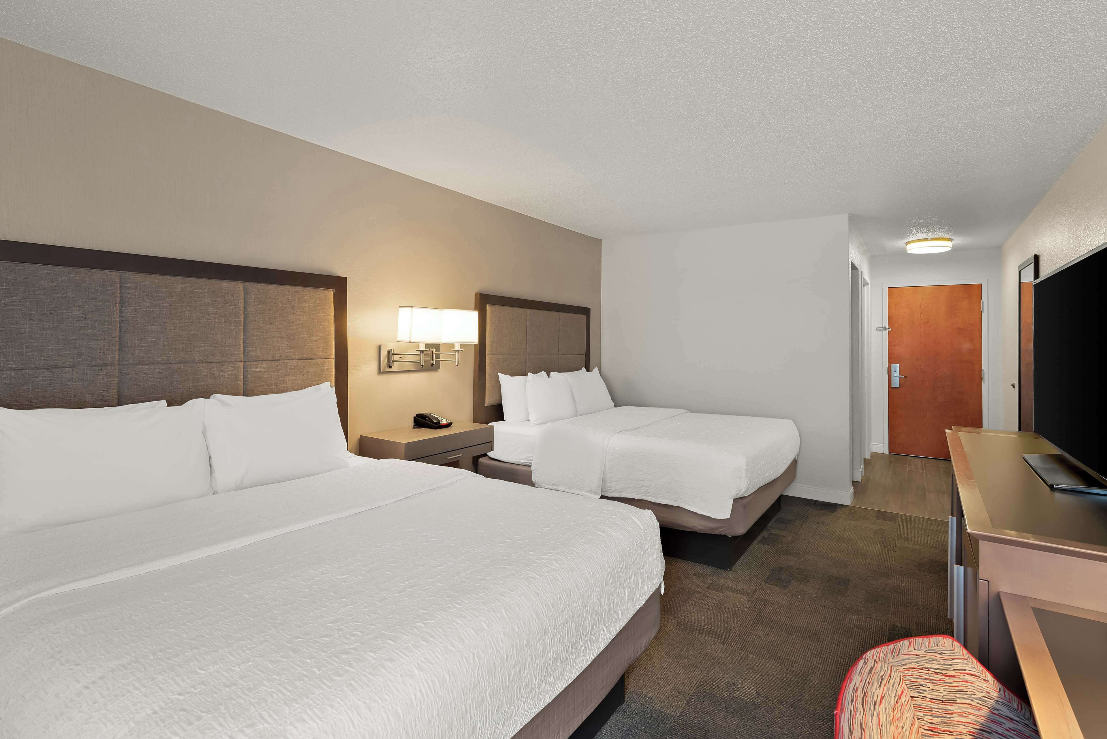 A hotel room with two beds, a desk, a TV, and a lamp.