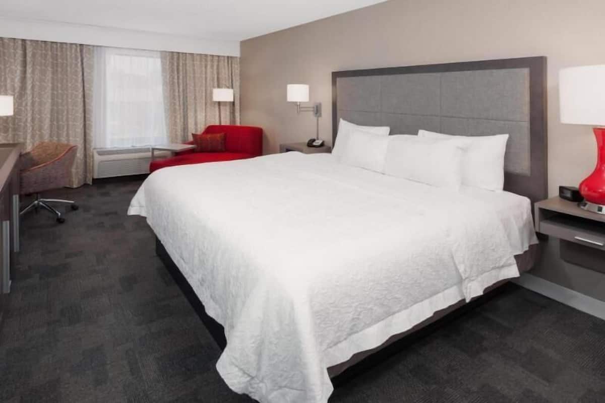 A hotel room with a large bed, a desk, a chair, and a red lamp.