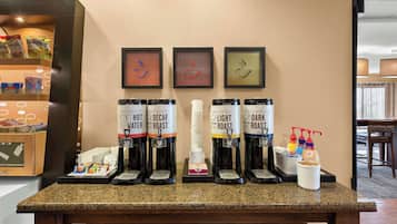 A coffee station with four coffee dispensers labeled 'Hot Water,' 'Decaf Roast,' 'Light Roast,' and 'Dark Roast.' There are also condiment dispensers and a small display of snacks.
