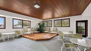A conference room with a wooden floor, white tables, and green chairs. There are large windows with views of the outside. - Hampton Inn Lancaster (Lancaster)