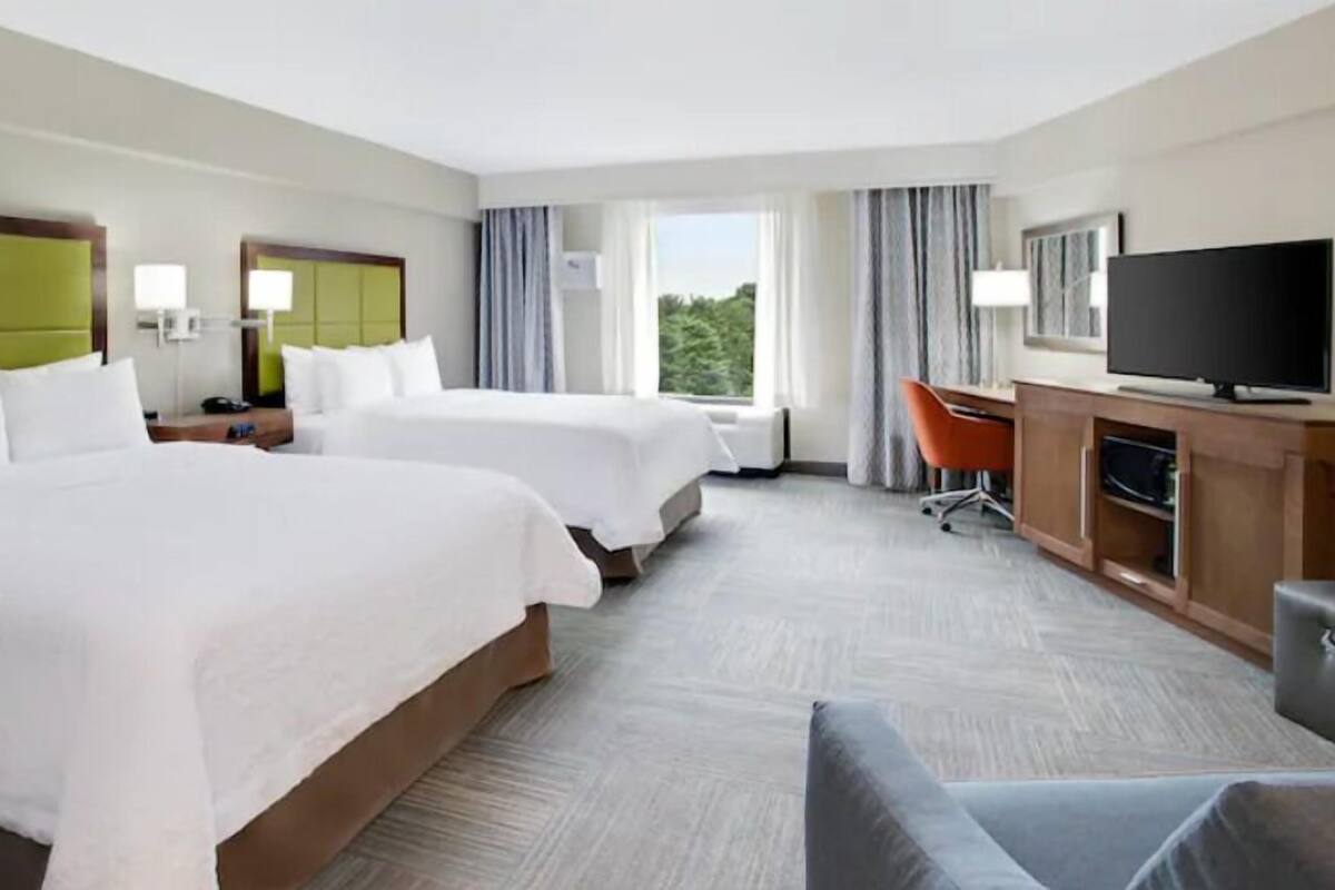 A hotel room with two beds, a desk, a chair, a television, and a window with curtains.