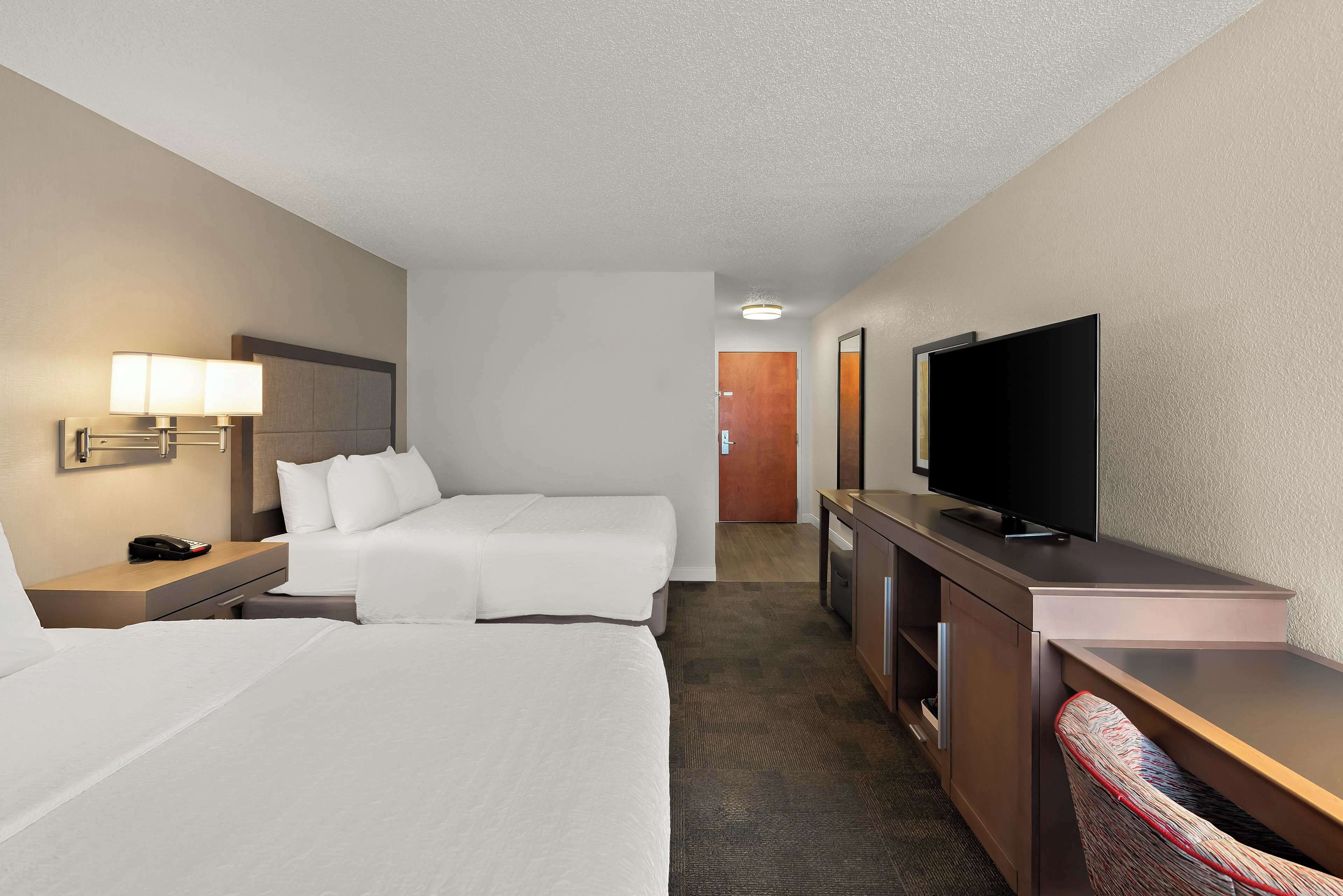 Habitación de hotel con dos camas, un escritorio, un televisor y la puerta del baño al fondo.