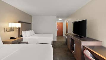 Habitación de hotel con dos camas, un escritorio, un televisor y la puerta del baño al fondo.