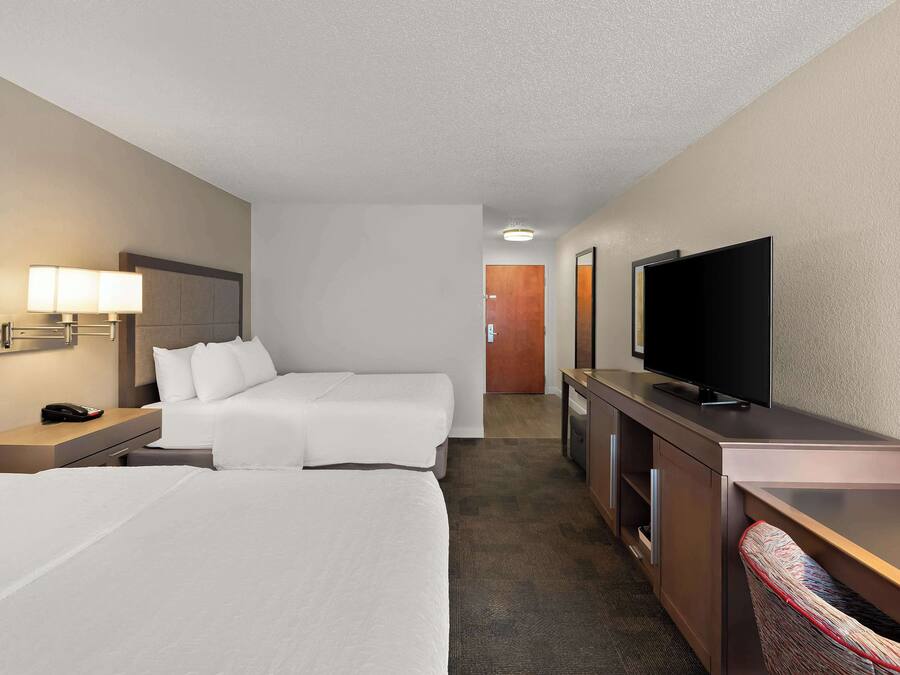 Habitación de hotel con dos camas, un escritorio, un televisor y la puerta del baño al fondo.
