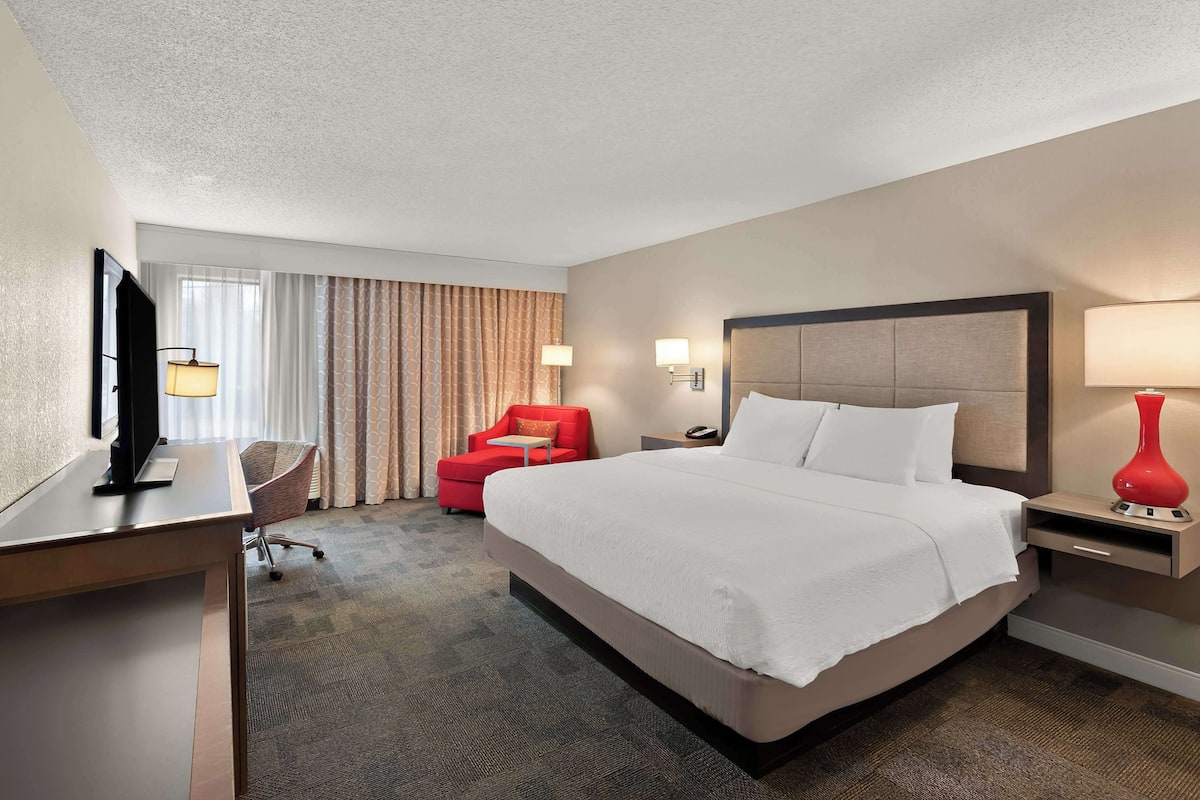 A hotel room with a large bed, a desk, a red armchair, and a TV.
