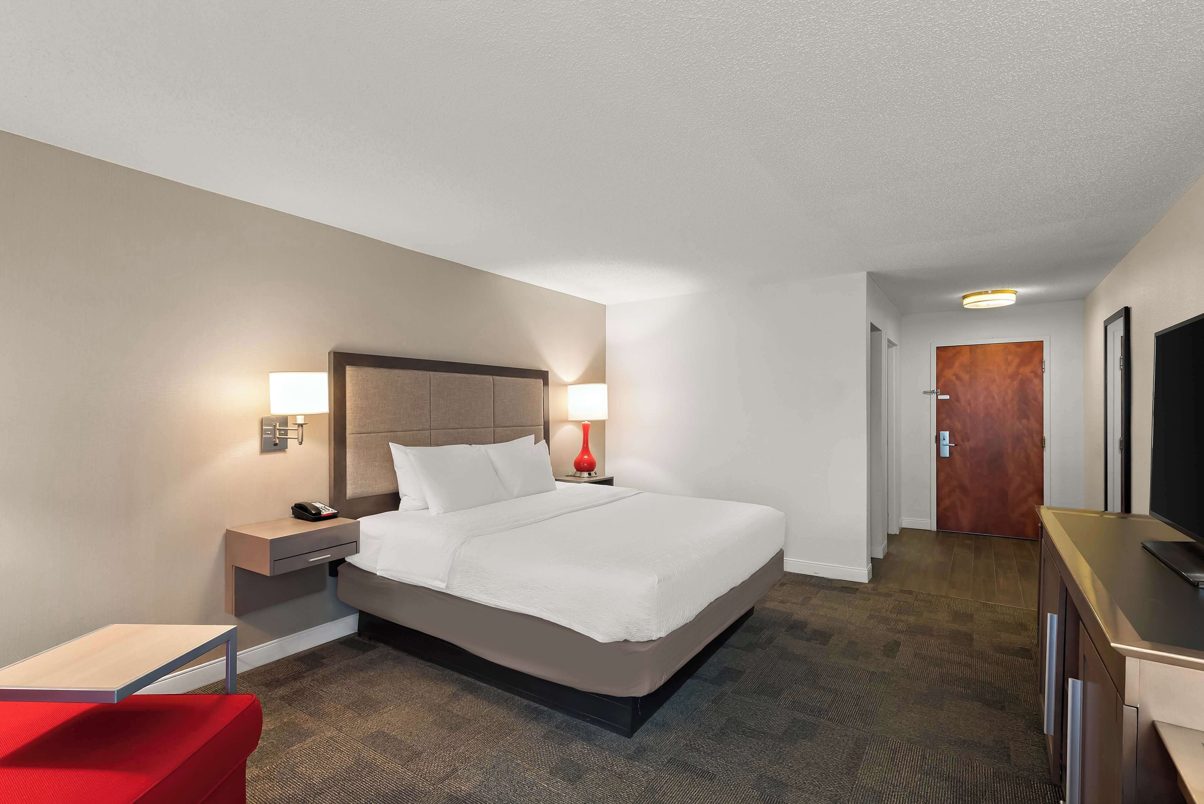 A hotel room with a bed, bedside tables, a desk, a chair, and a television.