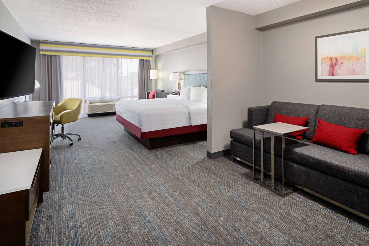A hotel room with a bed, a sofa, a desk, a TV, and a window with curtains.