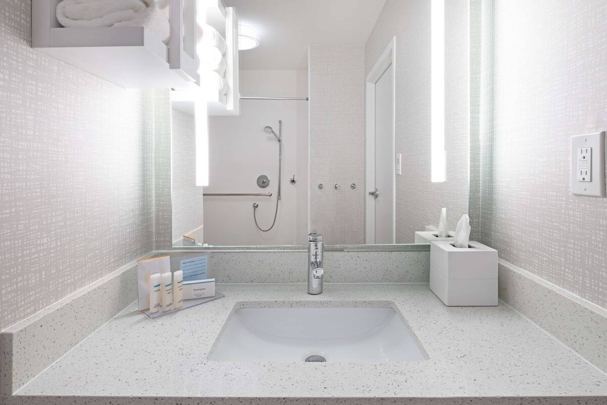 A bathroom with a large sink, a mirror, a shower, and a towel rack.
