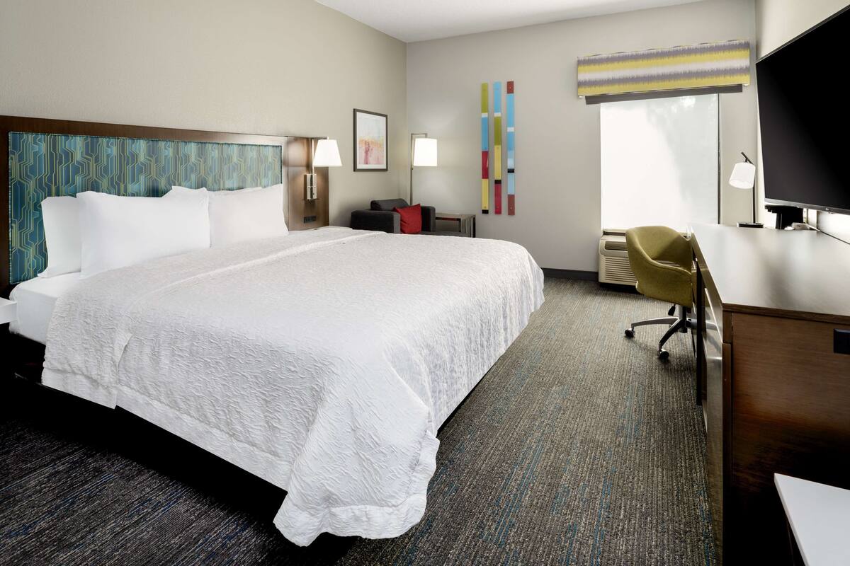 A hotel room with a large bed, a desk, a chair, and a television.