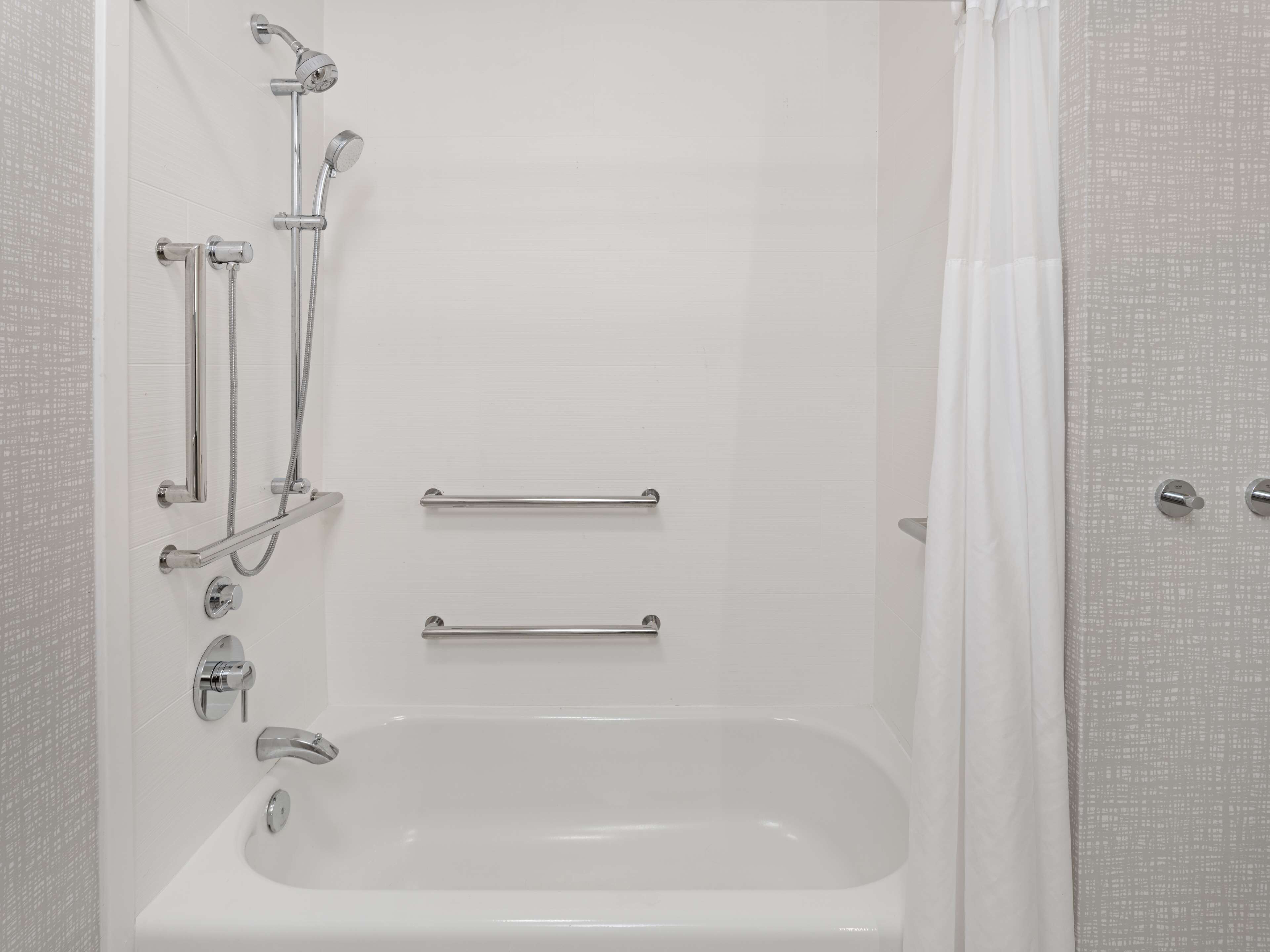 Une salle de bain moderne équipée d’une baignoire, de barres d’appui et d’un pommeau de douche.