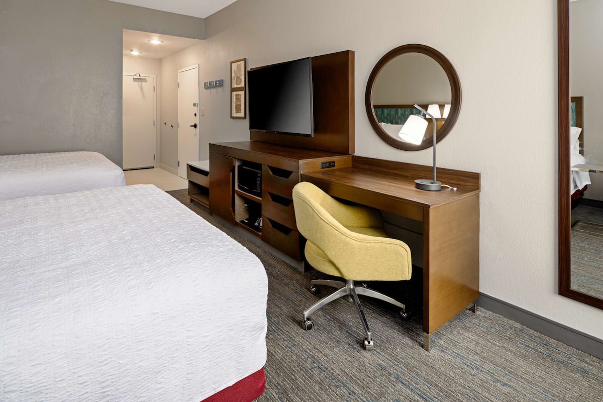 A hotel room with a bed, a desk with a chair, a television, a mirror, and a wardrobe.