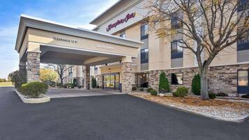 Un Hampton Inn con entrada despejada, fachada de piedra y un cartel de bienvenida.