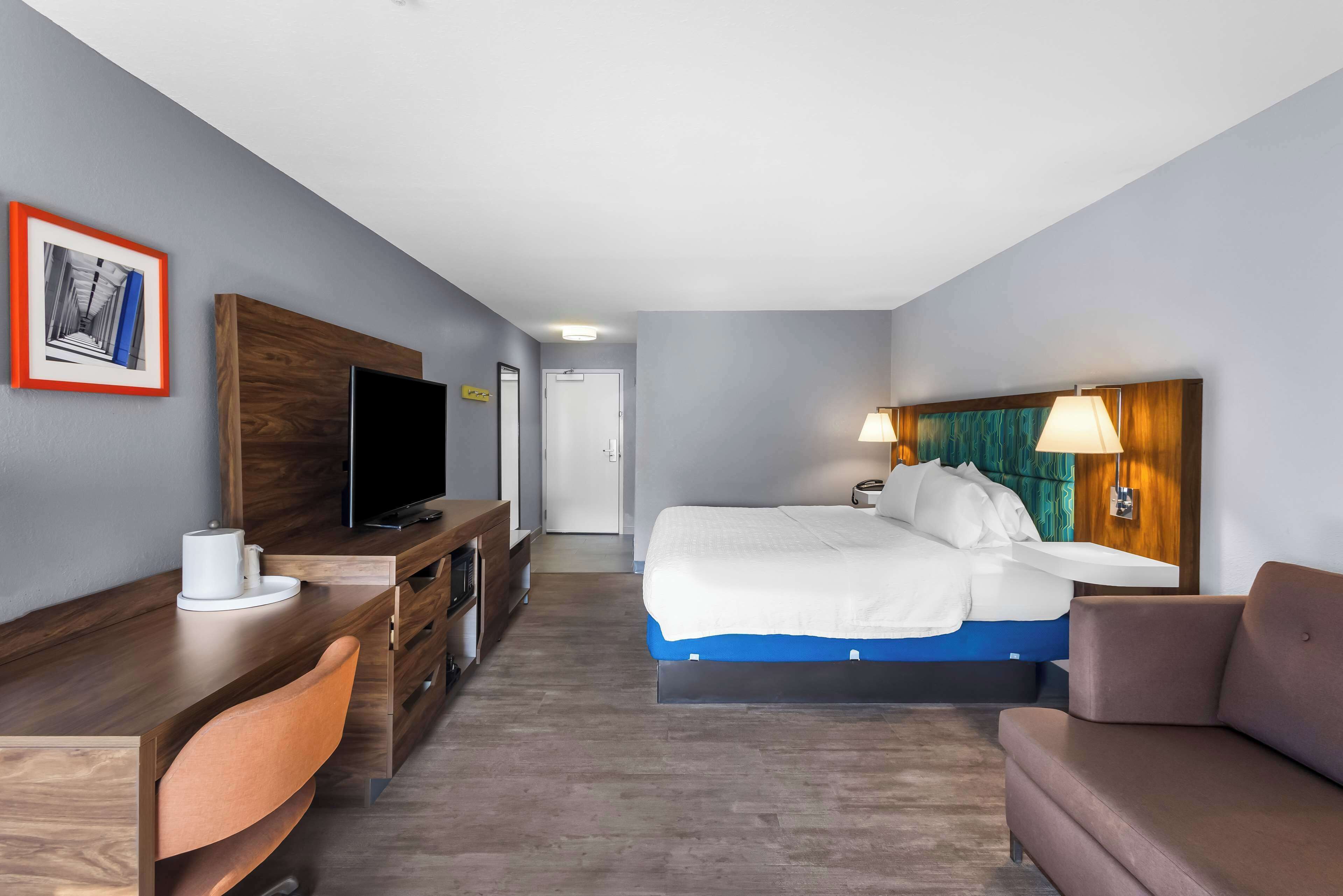 Ein Hotelzimmer mit Bett, Schreibtisch mit Fernseher, Stuhl und Lampe.