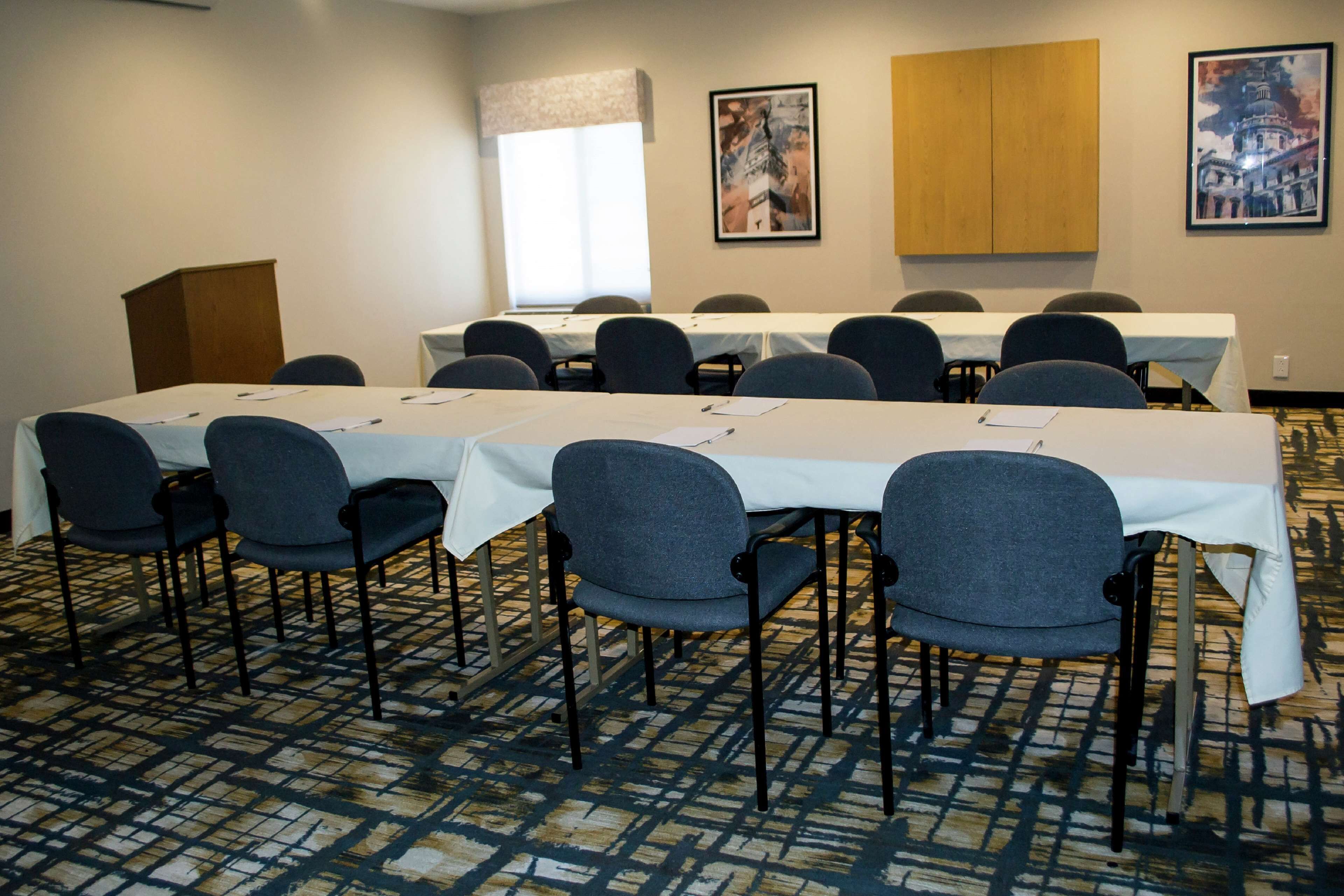 A conference room with a long table, multiple chairs, a podium, and framed pictures on the walls.
