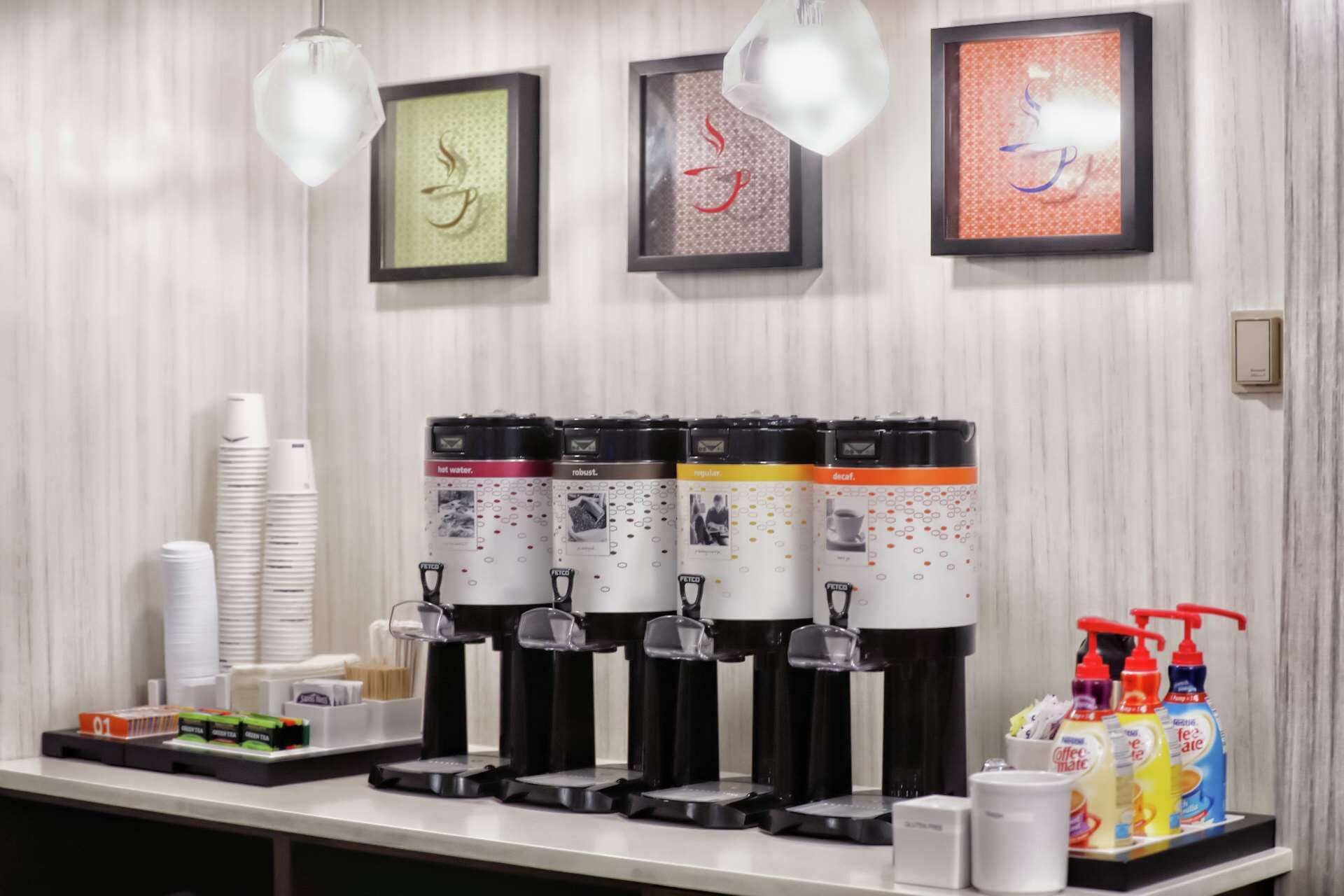 A coffee station with multiple dispensers, disposable cups, and a selection of beverages.