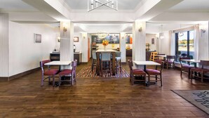 A spacious hotel lobby with a central dining area, multiple seating arrangements, and a modern chandelier. - Hampton Inn Marion (Marion)