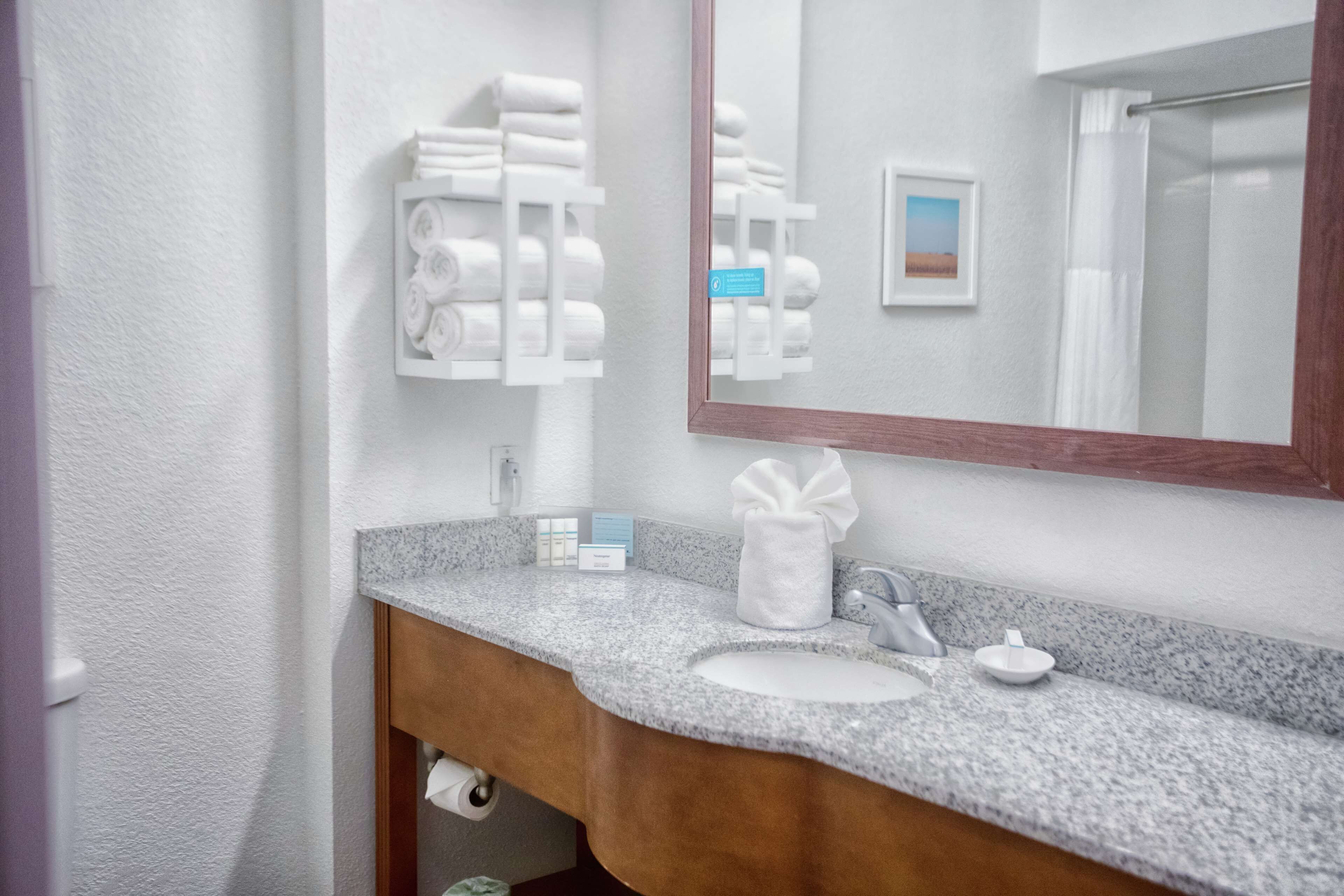 Une salle de bain dotée d’un comptoir en granit, d’un lavabo, d’un miroir et de porte-serviettes.